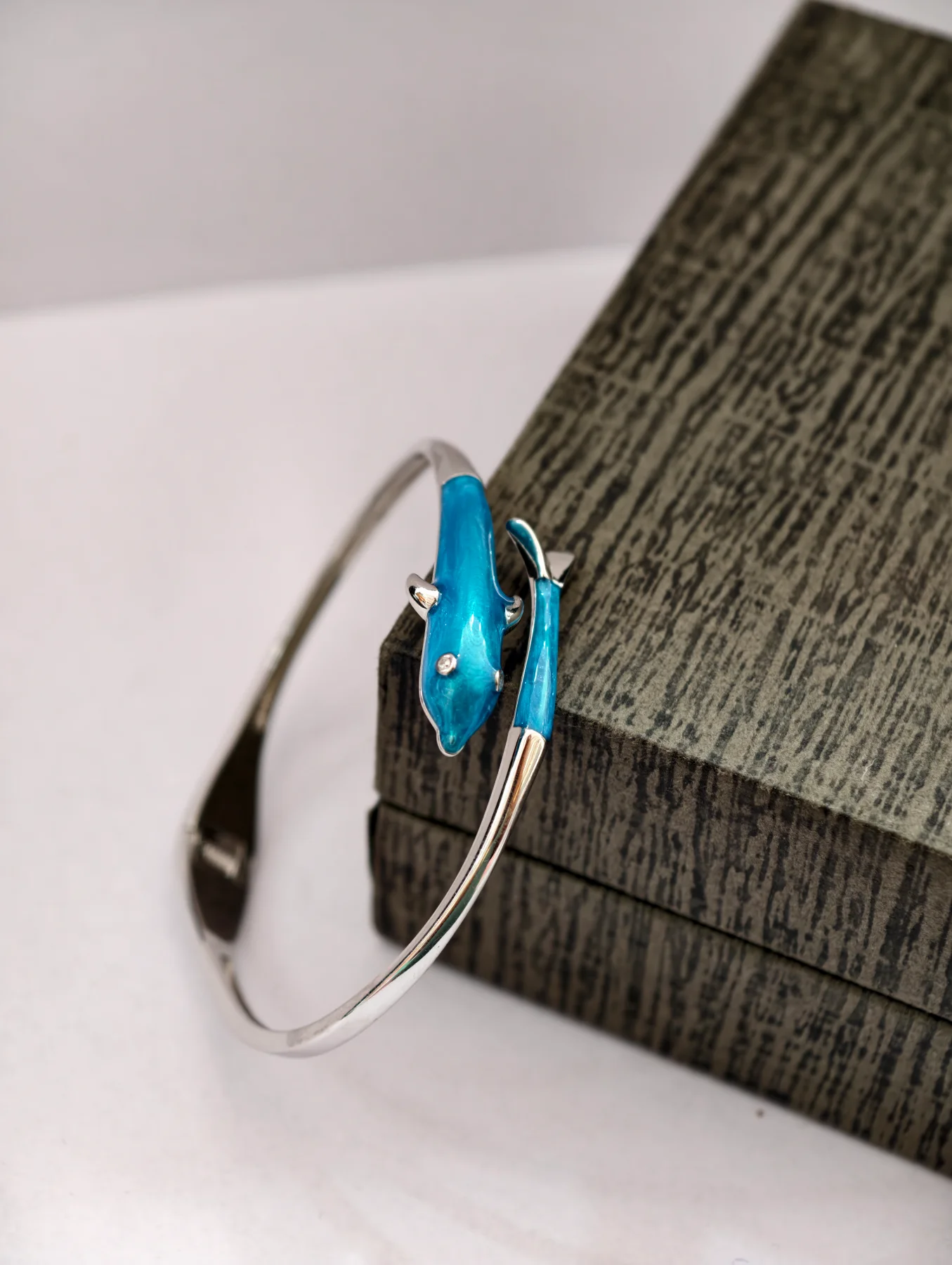 Glossy silver bracelet featuring a blue dolphin motif with a single small white stone.