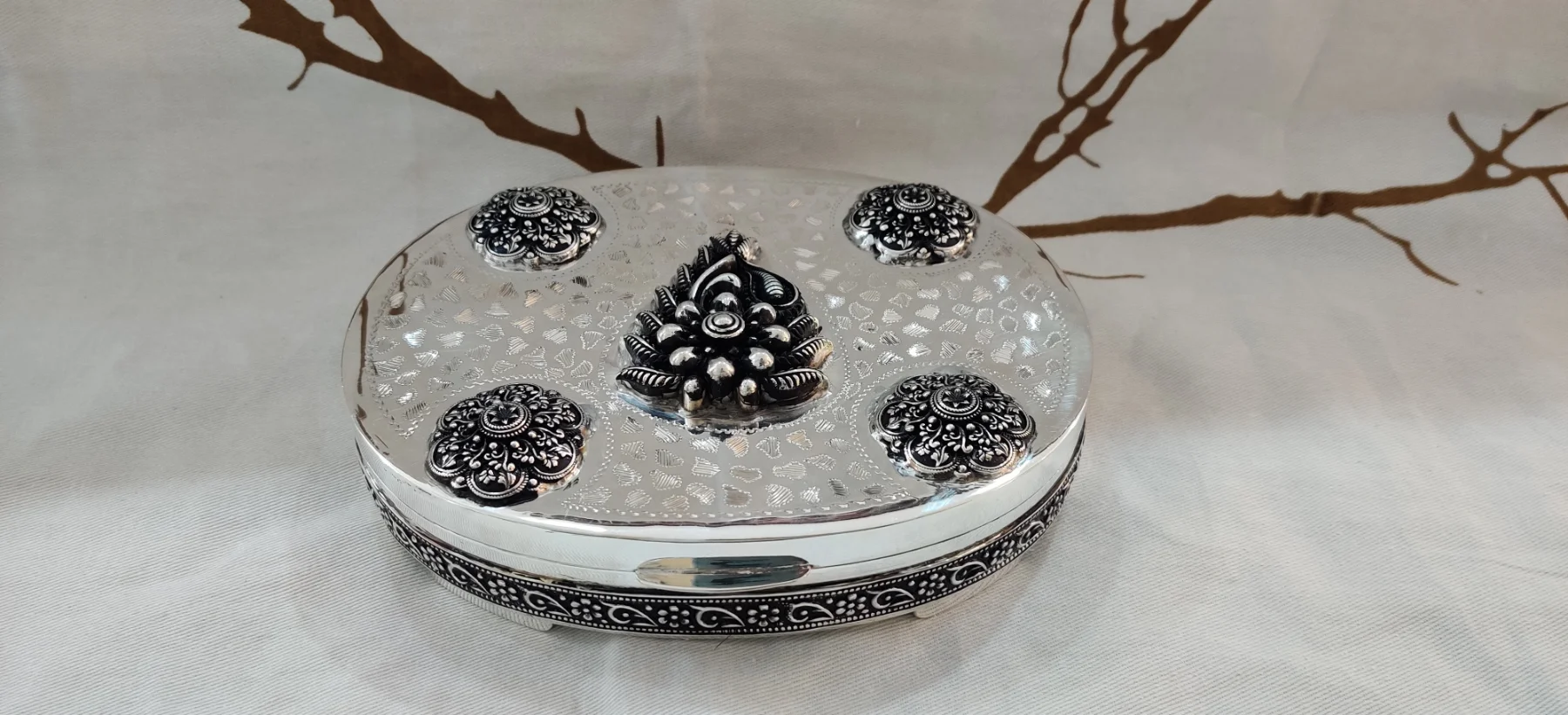 An oval silver betel nut set featuring ornate floral patterns and textured work with oxidised finish.
