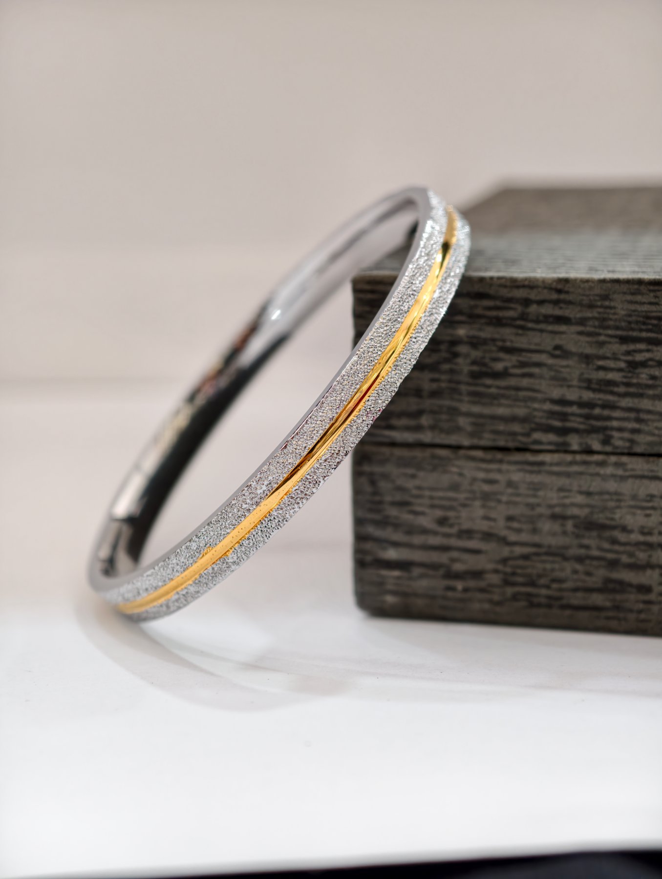 A flat silver kada featuring a textured sparkling finish and a central polished gold line.