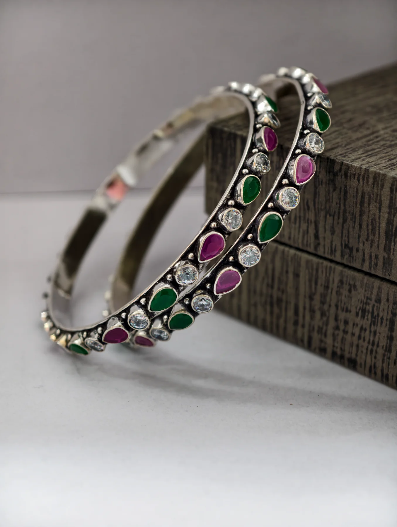 Oxidised silver bangles feature alternating round white stones and teardrop pink and green stones.