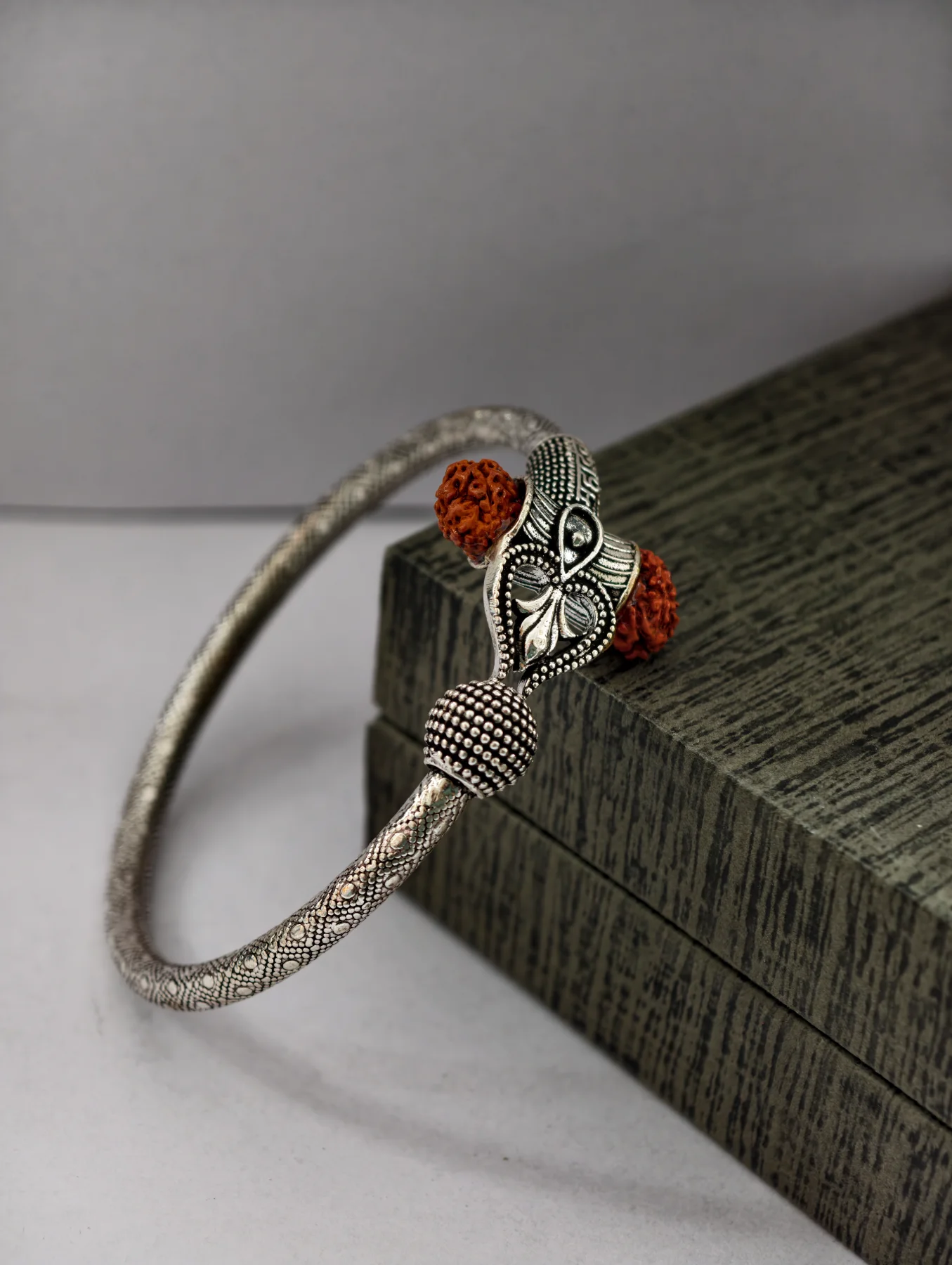 Oxidised silver kada featuring a Trishul design with brown rudraksha beads and textured patterns along the band.