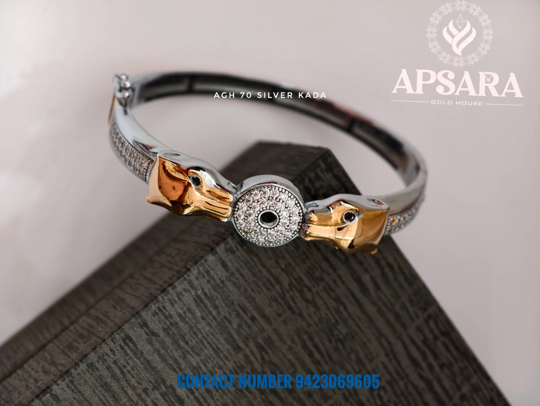 This silver kada features two golden animal heads facing a circular central motif encrusted with white stones.