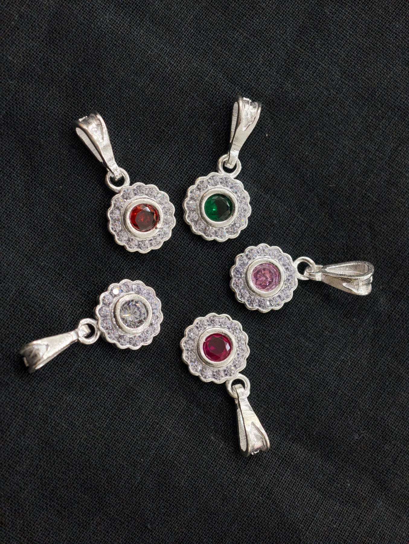 Small round silver lockets featuring a central coloured stone surrounded by a scalloped border of tiny white stones.
