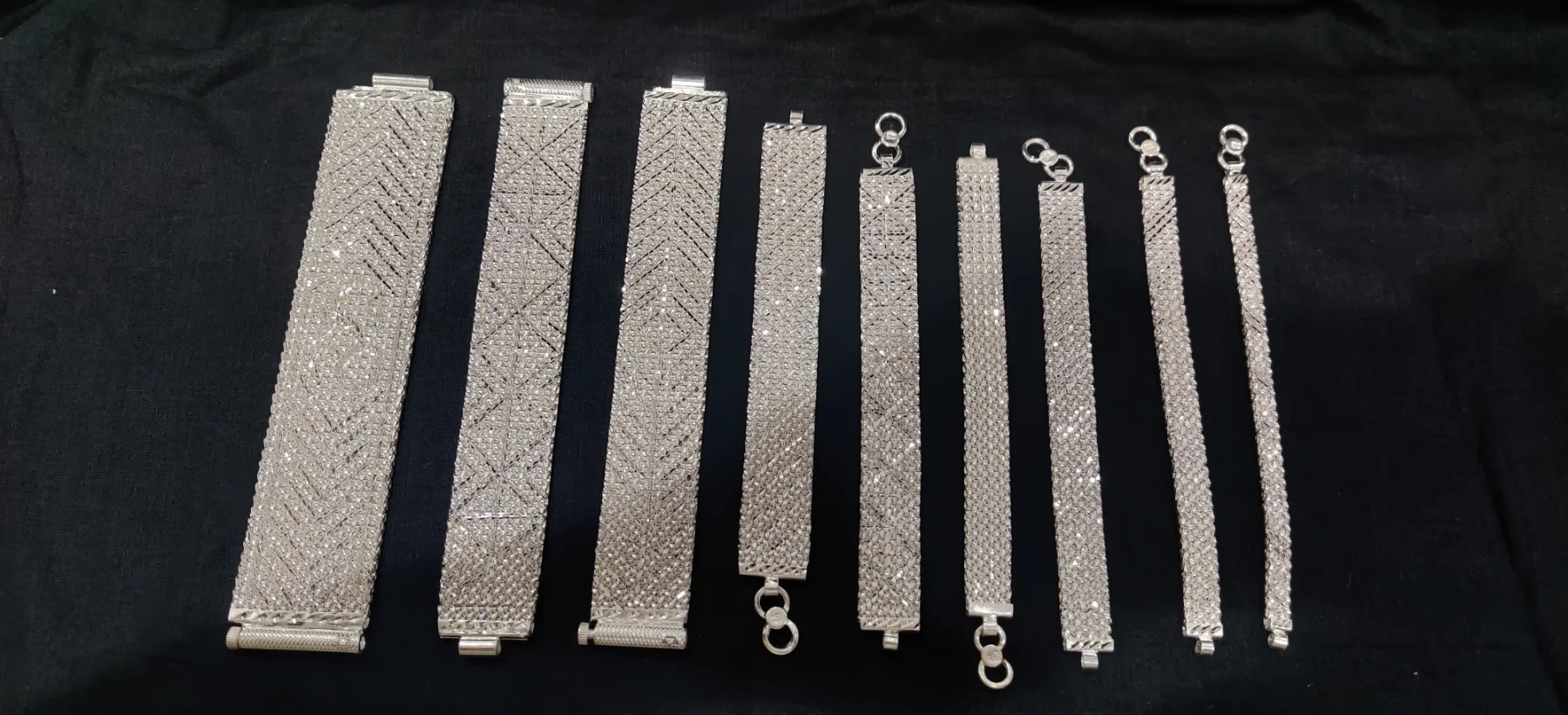 A collection of wide silver bracelets featuring various geometric cut work and textured chevron patterns in a shiny finish.