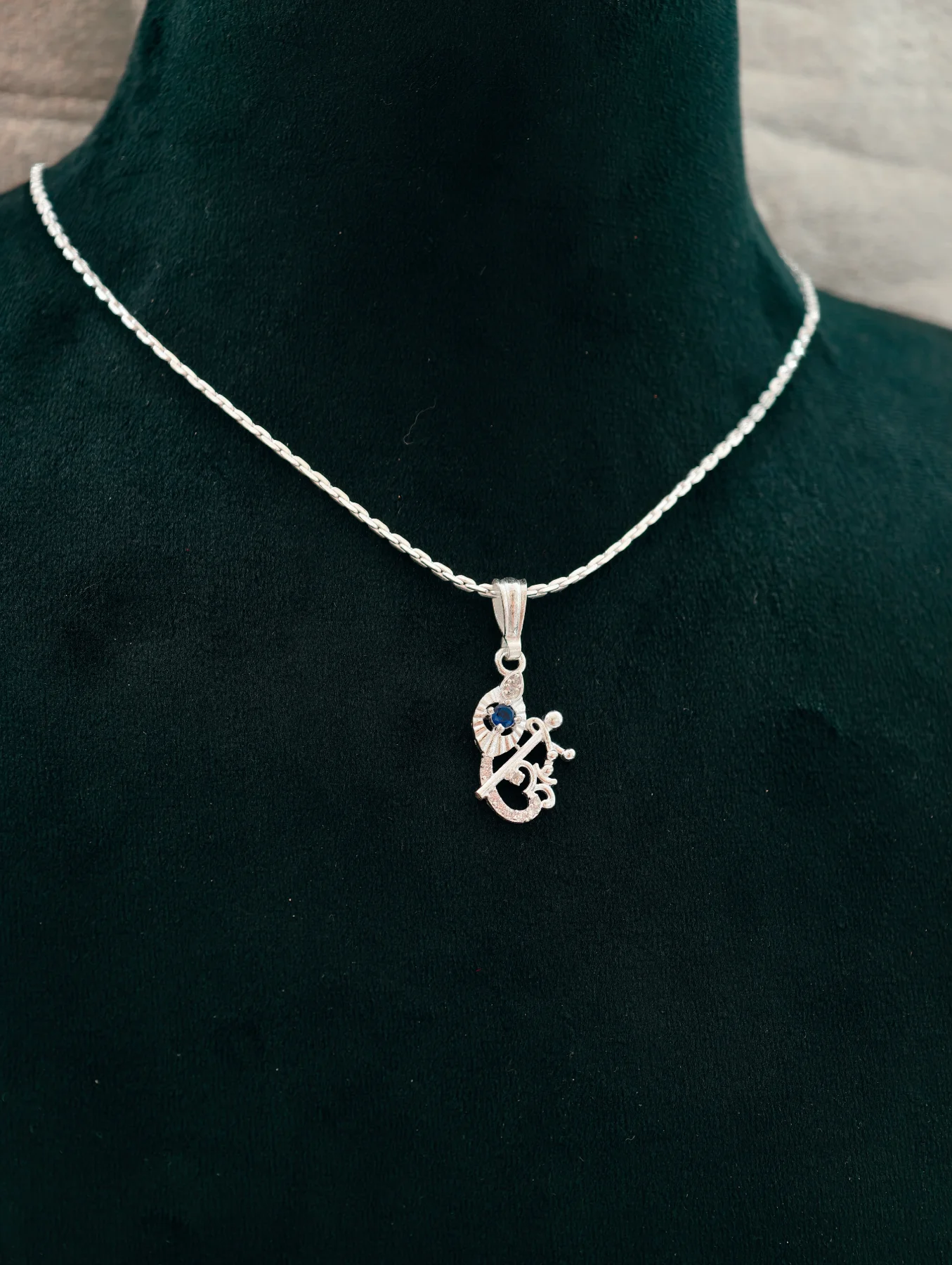 Silver chain with a Lord Krishna locket featuring a blue stone and an om symbol.