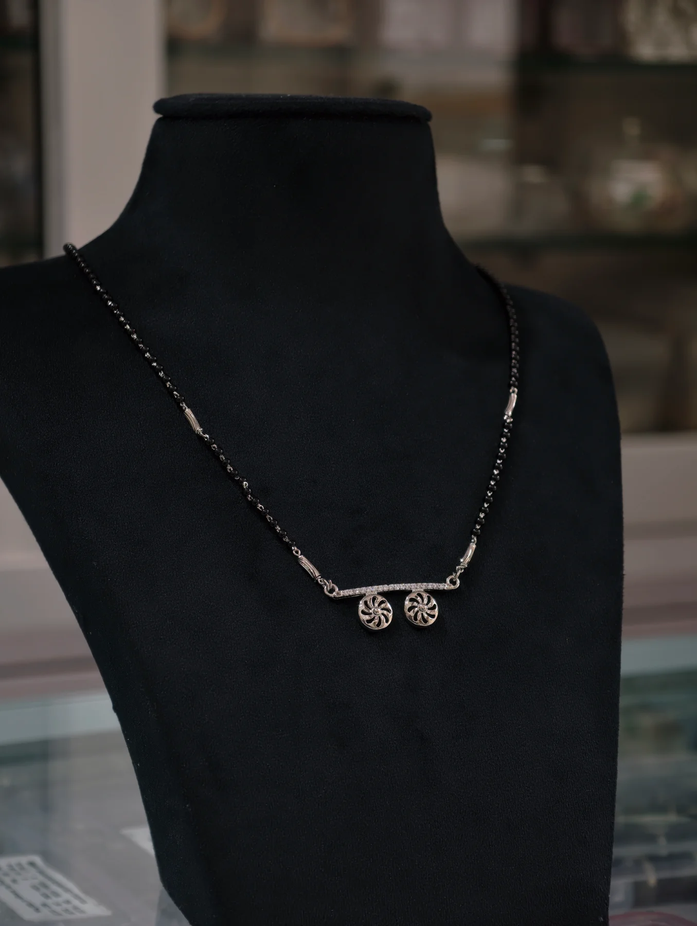 An elegant silver mangalsutra featuring black bead chains and two round hanging pendants with white stones.