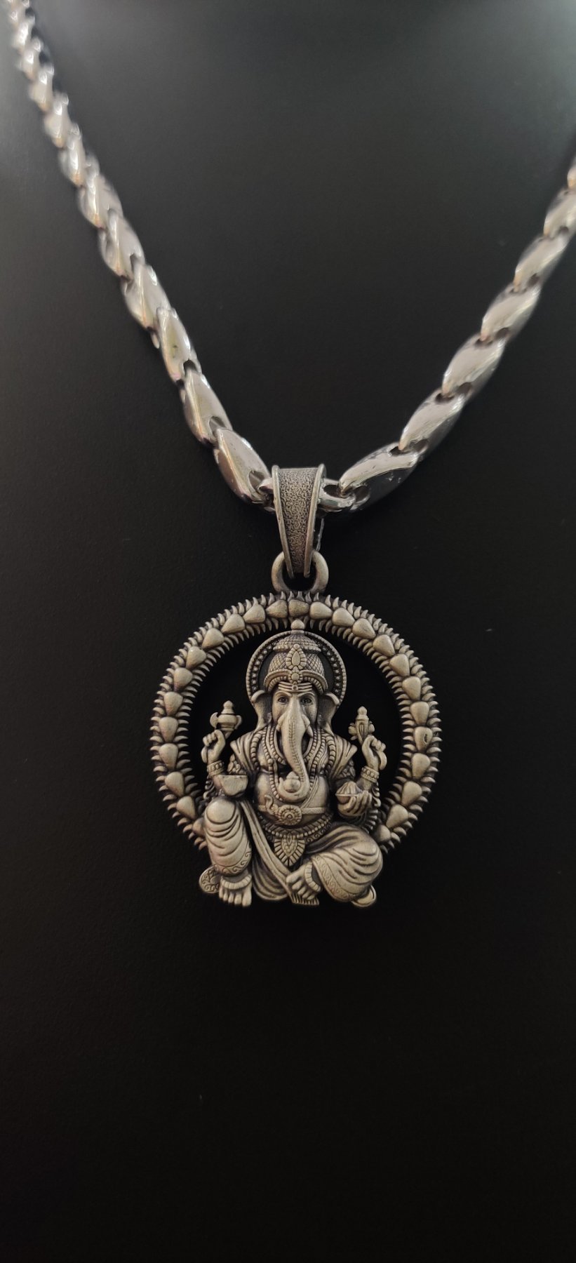 An oxidised silver chain with a round Ganesha locket featuring detailed carving and a textured border.