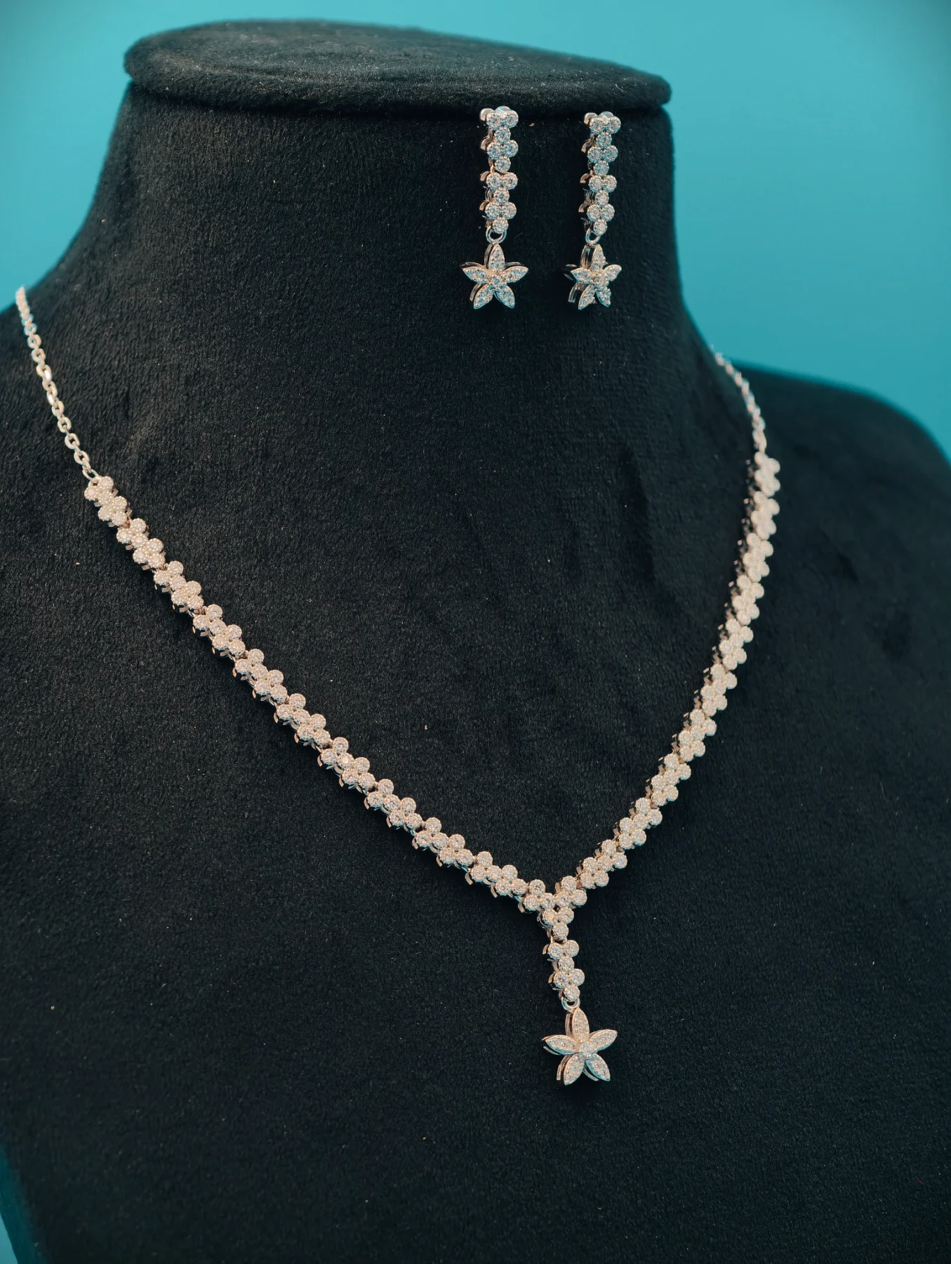 This silver necklace and earring set features a delicate floral pattern with sparkling white stones arranged in linear motifs.