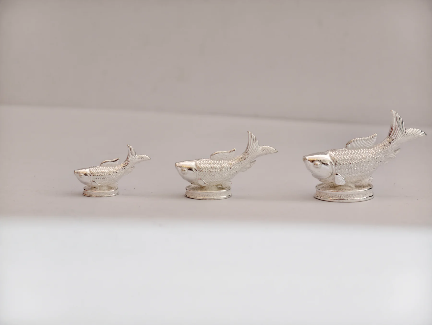 Three silver fish idols with textured scales and round bases, showing a polished finish.