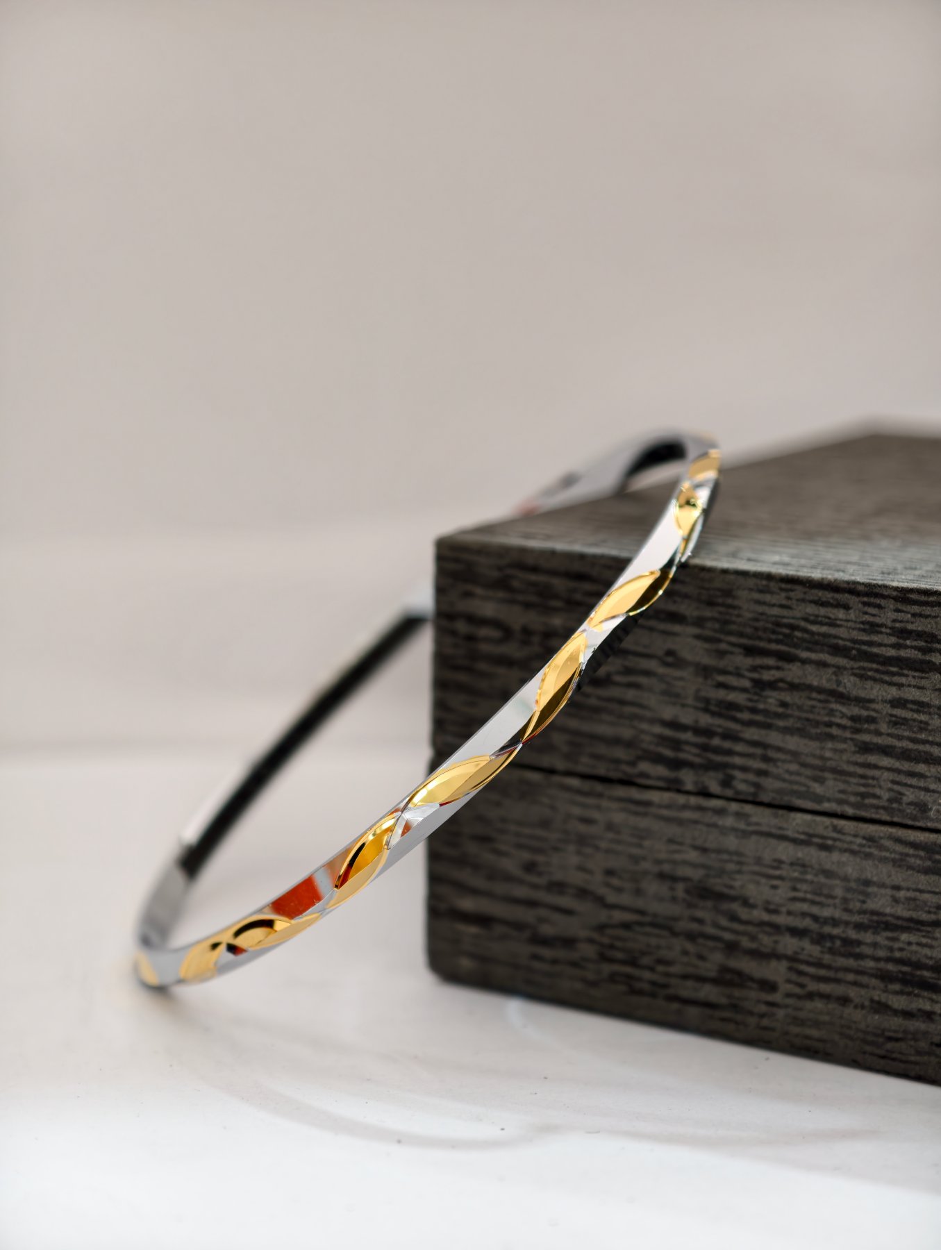 A slim silver kada featuring an alternating shiny leaf pattern with gold polish finish.
