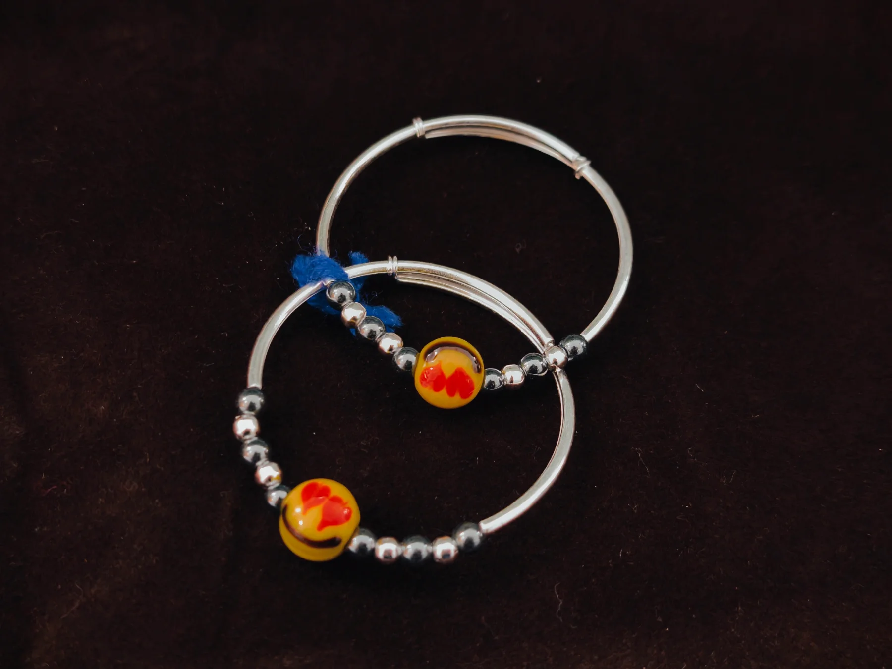 Silver kada pair featuring glossy silver beads and a central yellow bead with red heart pattern.