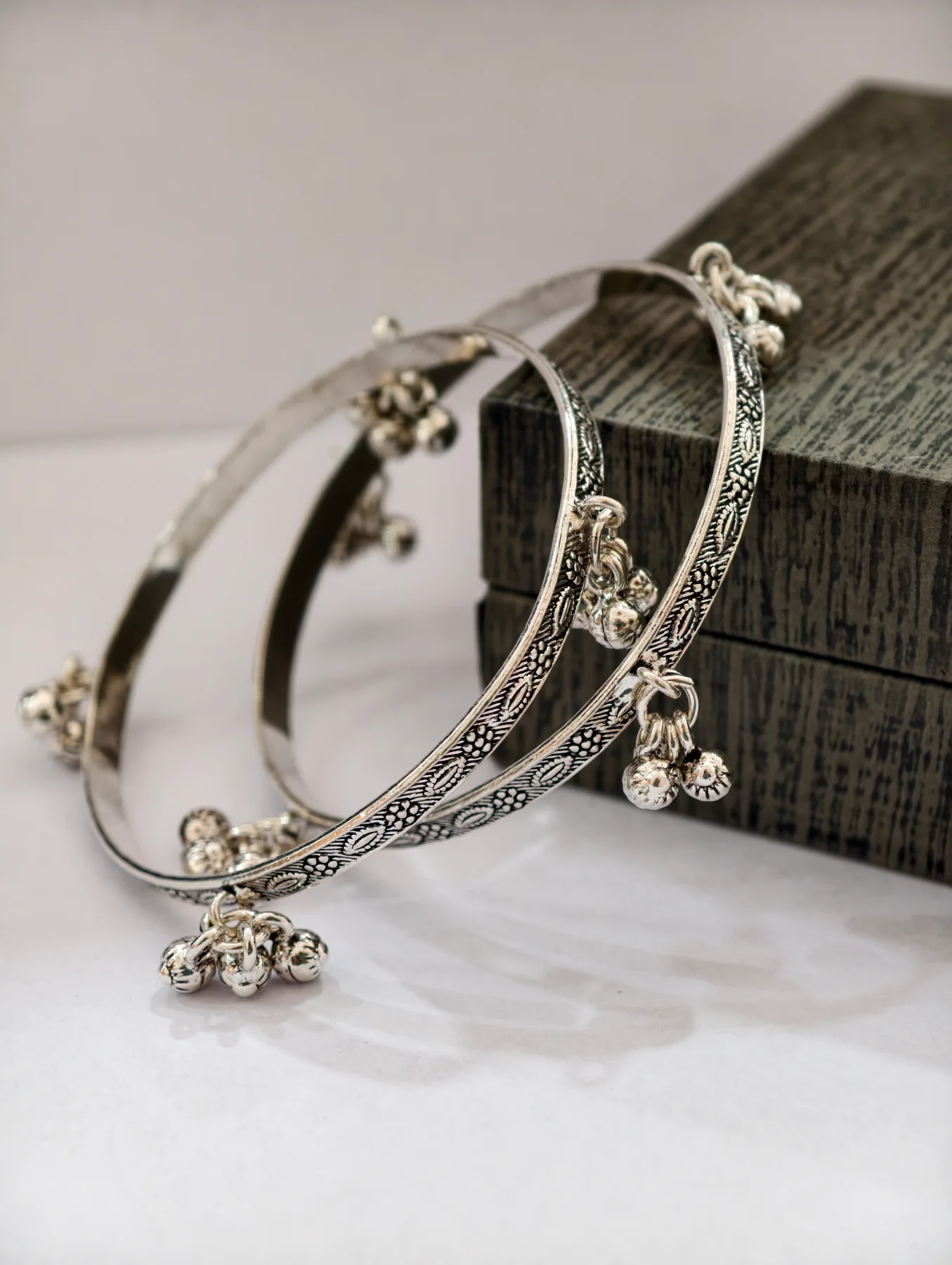 Silver oxidised kada bangles featuring intricate engraved floral patterns and hanging ghungroo bells.