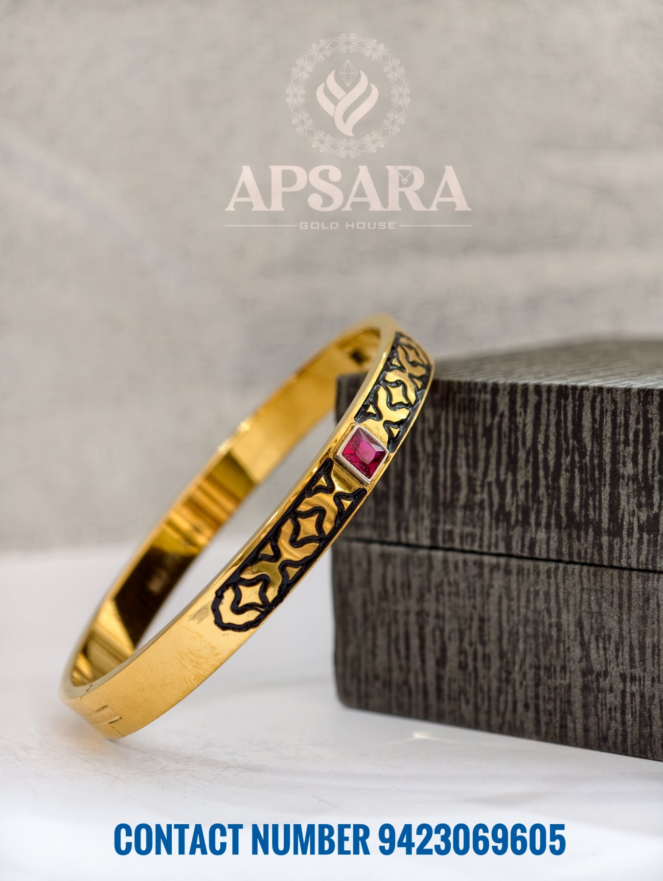 A gold polished silver men's kada with black patterns and a red square stone.