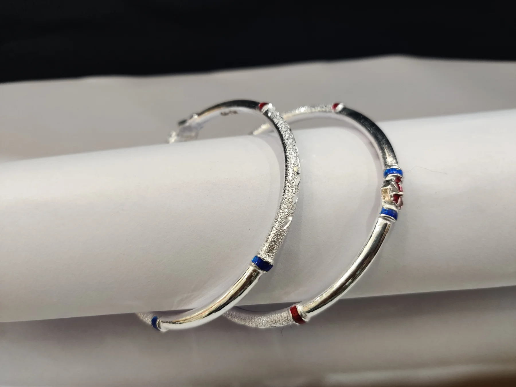 Silver bangles featuring textured patterns and colorful enameled highlights along the smooth metal body.