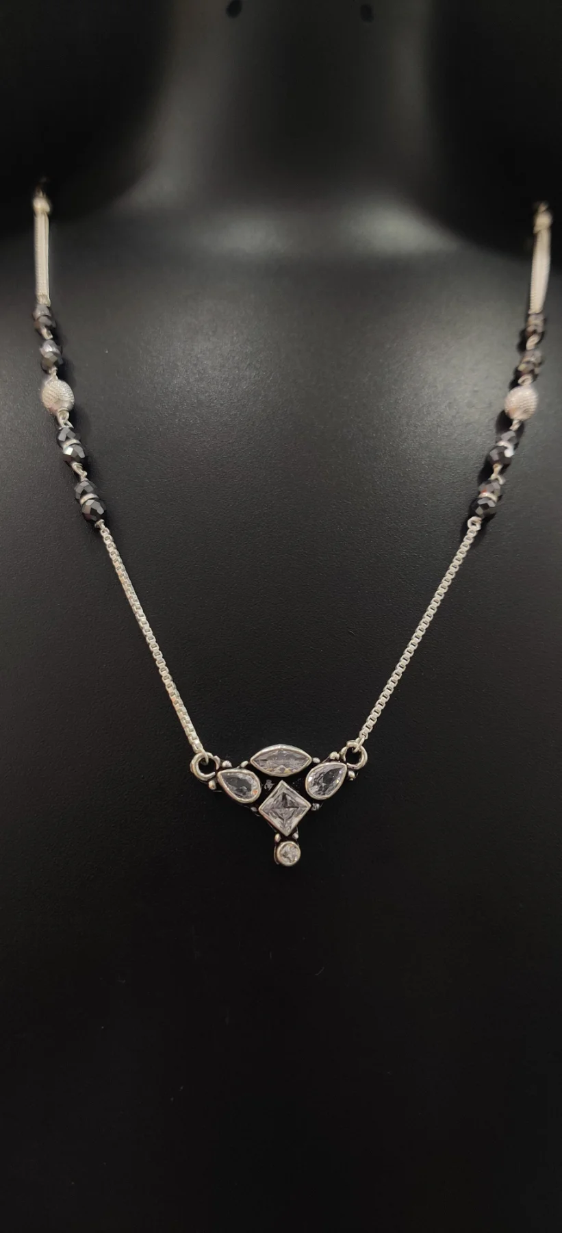A delicate oxidised silver mangalsutra featuring a geometric pendant with white stones and black beaded chain details.