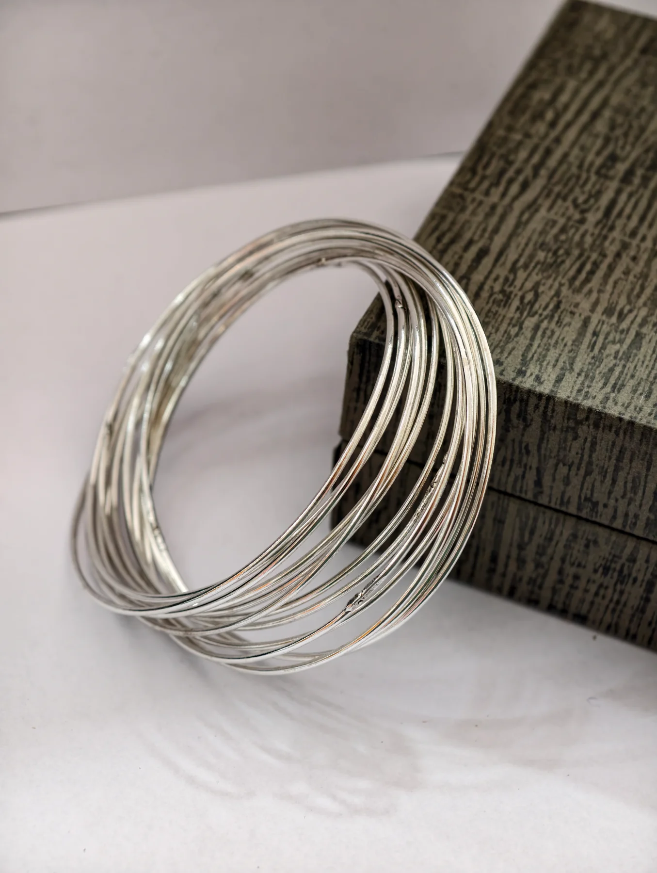 These round silver bangles feature a plain interlocking multi wire design with a shiny finish.