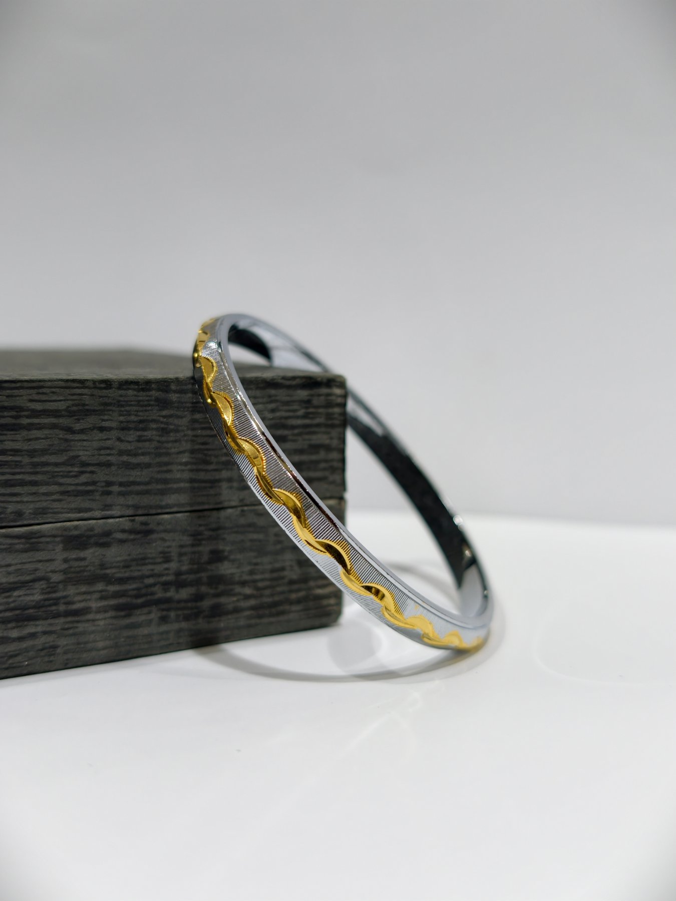 A silver Punjabi kada featuring a textured pattern with a wavy gold polish design.