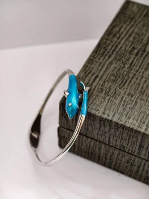 Glossy silver bracelet featuring a blue dolphin motif with a single small white stone.
