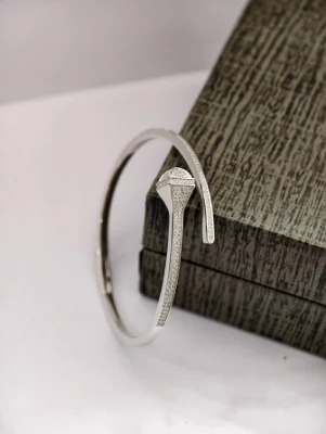 A modern silver open bracelet featuring a geometric nail head design encrusted with small white stones.