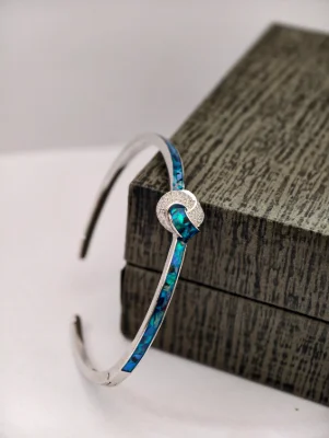 Silver bracelet with blue mosaic inlay and a round stone studded knot motif.