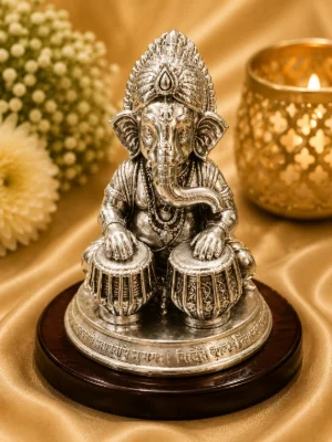 Detailed silver idol of Lord Ganesha playing tabla instruments with intricate carvings and traditional crown.