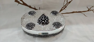 An oval silver betel nut set featuring ornate floral patterns and textured work with oxidised finish.
