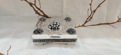 An oxidised silver betel nut set features intricate floral carvings and ornate corner motifs on a square body.