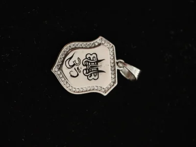 This shield shaped silver locket features a black engraved Om and Trishul symbol bordered by a line of sparkling white stones.