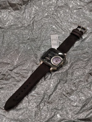 Silver luxury watch with a square stone studded dial and a brown leather strap.