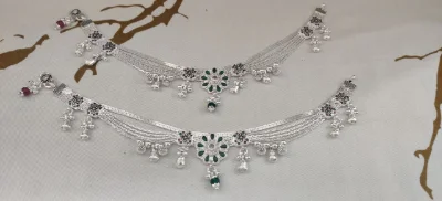 These multi-strand silver payals feature a central floral motif with green stones and hanging silver bells.