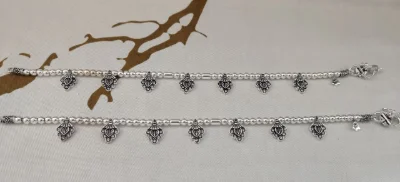 Silver fancy payal with small beads and dangling leaf shaped charms featuring intricate patterns.