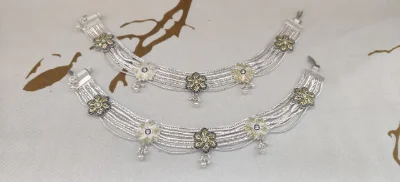 A pair of multi-strand silver payal featuring floral motifs with gold accents, delicate leaf patterns, and small hanging dangles.