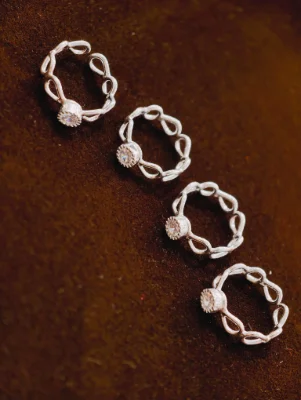 Four silver bichiya featuring intricate loop patterns and a single round white stone set in each piece.