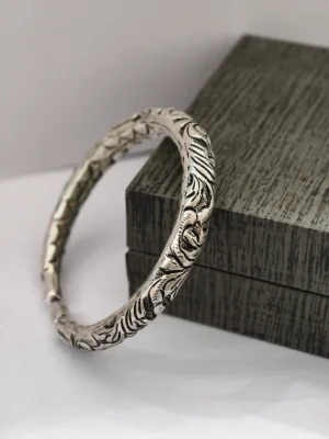 Oxidised silver kada with intricate traditional floral carvings and a classic round shape.