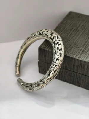 Oxidised silver kada with intricate floral pattern and plain curved ends.