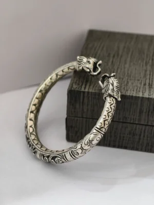 An oxidised silver kada with intricate traditional patterns and detailed animal head ends.