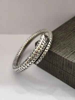 A silver kada featuring a textured scale pattern and an overlapping snake head design with an oxidised finish.