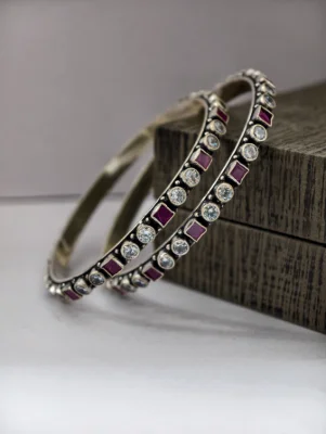 Oxidised silver bangles feature alternating round white stones and square red stones in a sleek pattern.