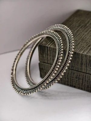Pair of oxidised silver bangles featuring detailed beaded rims and intricate patterns on silver metal.