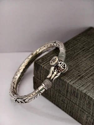 Oxidised silver kada featuring a trishul motif with om symbol and intricate leaf patterns along the band.
