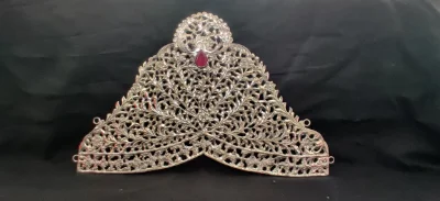 A silver crown features intricate floral filigree work and a central red stone.