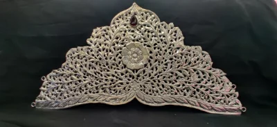 This intricate silver crown features detailed floral and leaf jali work with a central flower motif and red stone.