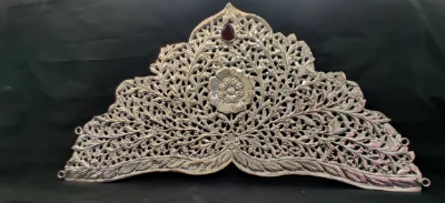 This intricate silver crown features detailed floral jaal work with a central flower and a dark gemstone.