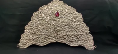 This silver crown features intricate floral carvings and a central red stone set near the top.
