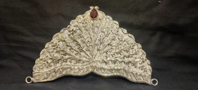 An ornate silver crown featuring detailed floral engraving and a single central red gemstone.