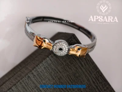 This silver kada features two golden animal heads facing a circular central motif encrusted with white stones.