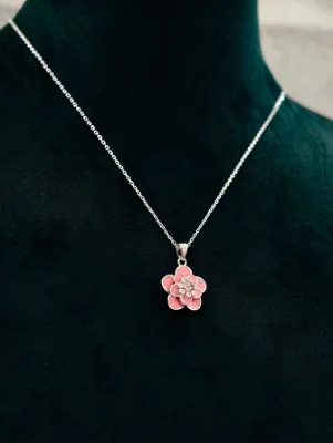 A silver chain with a pink flower locket having small white stones in the center.