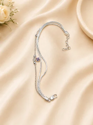 A delicate silver bracelet featuring layered chains, smooth metal beads, and a tiny floral charm with blue and red stones.