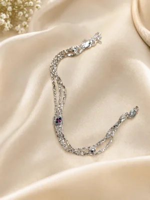 This shiny silver bracelet features three flexible chains with a small gemstone center piece and a dangling ball charm.