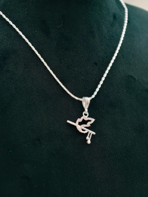 A silver locket in the shape of a flute and peacock feather hanging on a simple silver chain.
